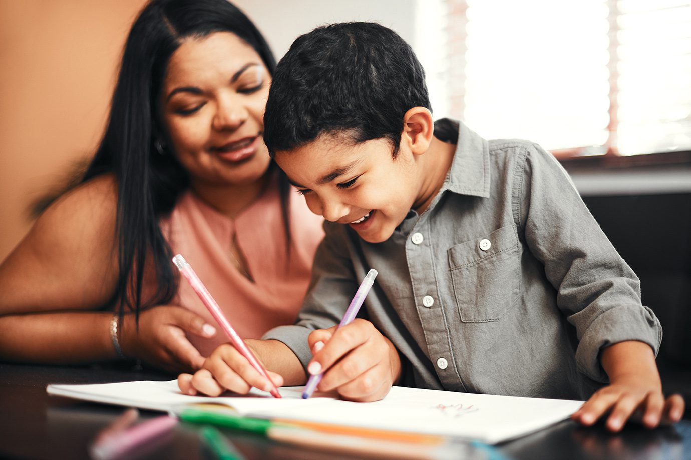 Child, colouring and woman with book in home, creativity activity and playful for kids development or drawing. Bonding, mother and table or learning with family together, happiness and colour pencils.